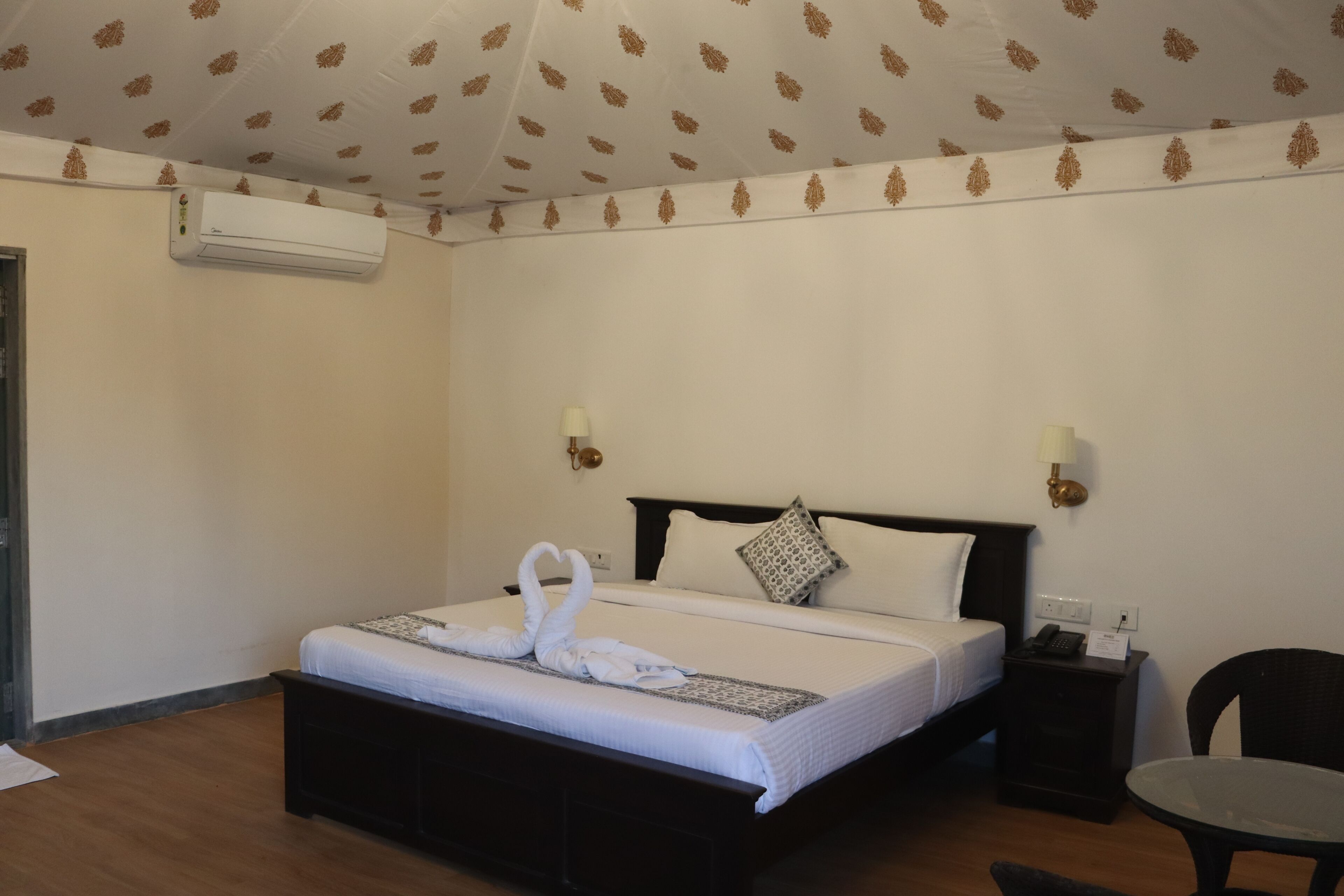 A hotel room with a bed, bedside tables, a chair, an air conditioning unit, and a patterned ceiling.