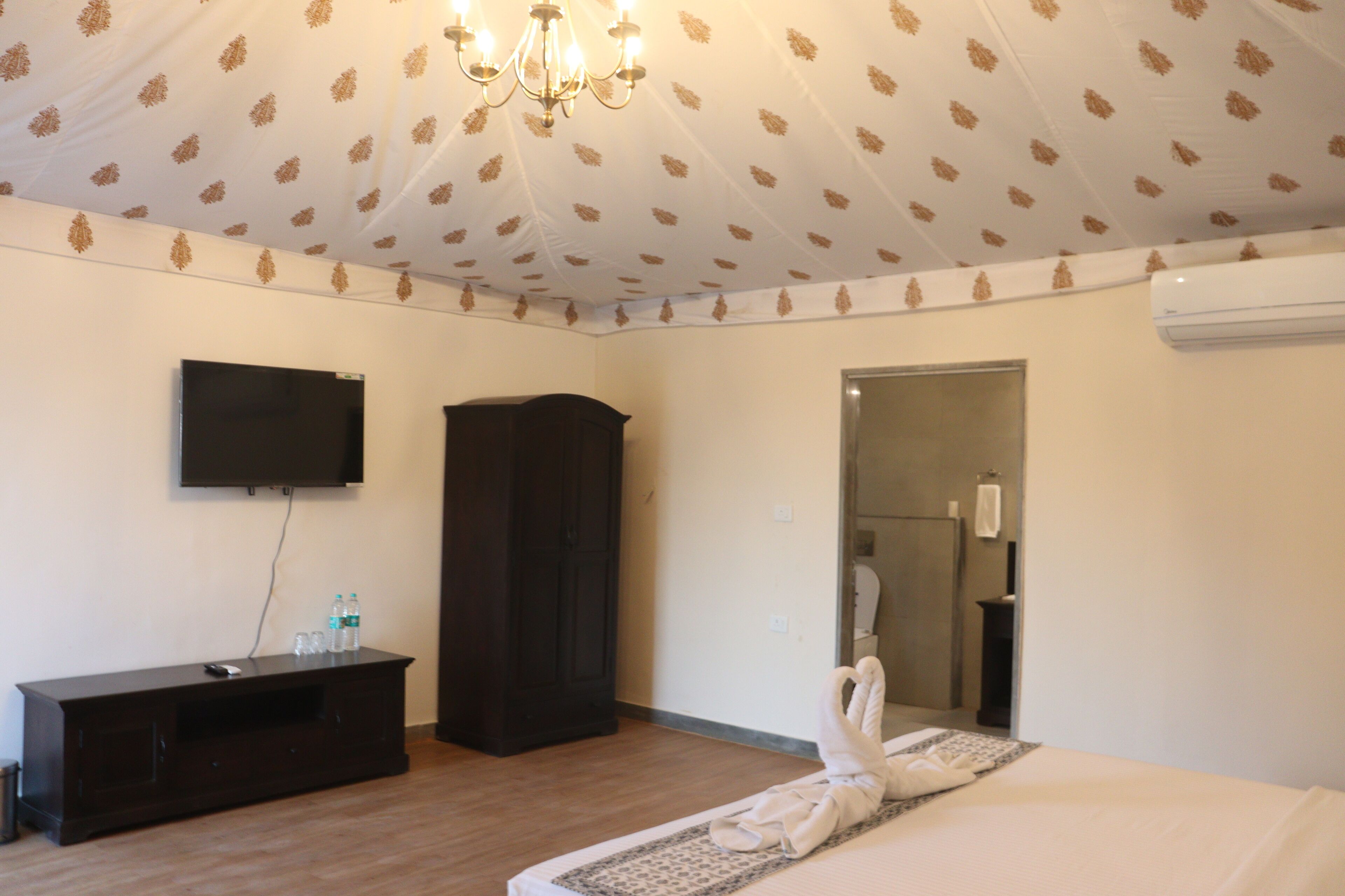 Une chambre d’hôtel avec un plancher en bois, un téléviseur à écran plat fixé au mur, une armoire de couleur sombre et un lit sur lequel est posée une serviette.