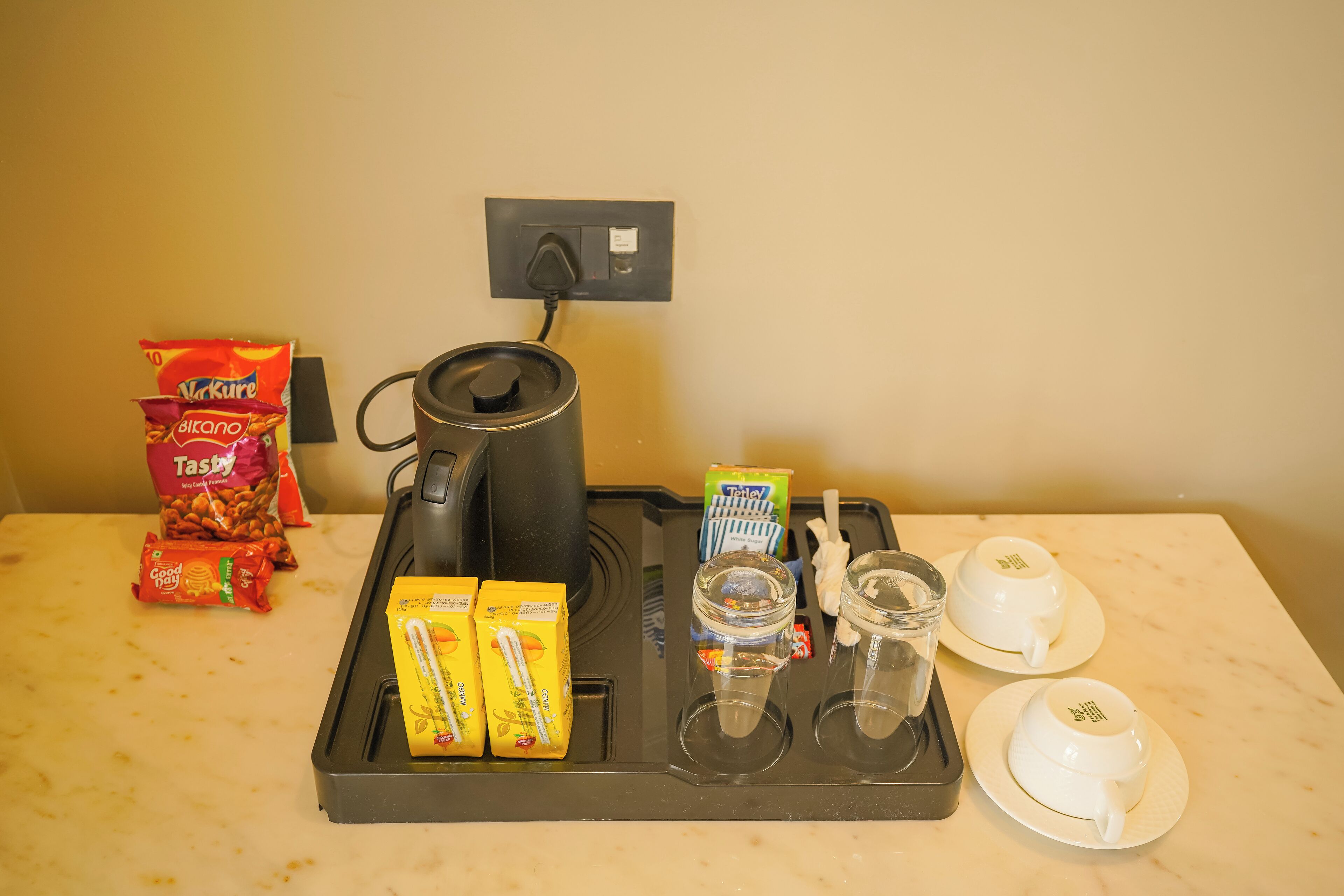 A breakfast tray with a coffee maker, two cups, a glass, and various food items.