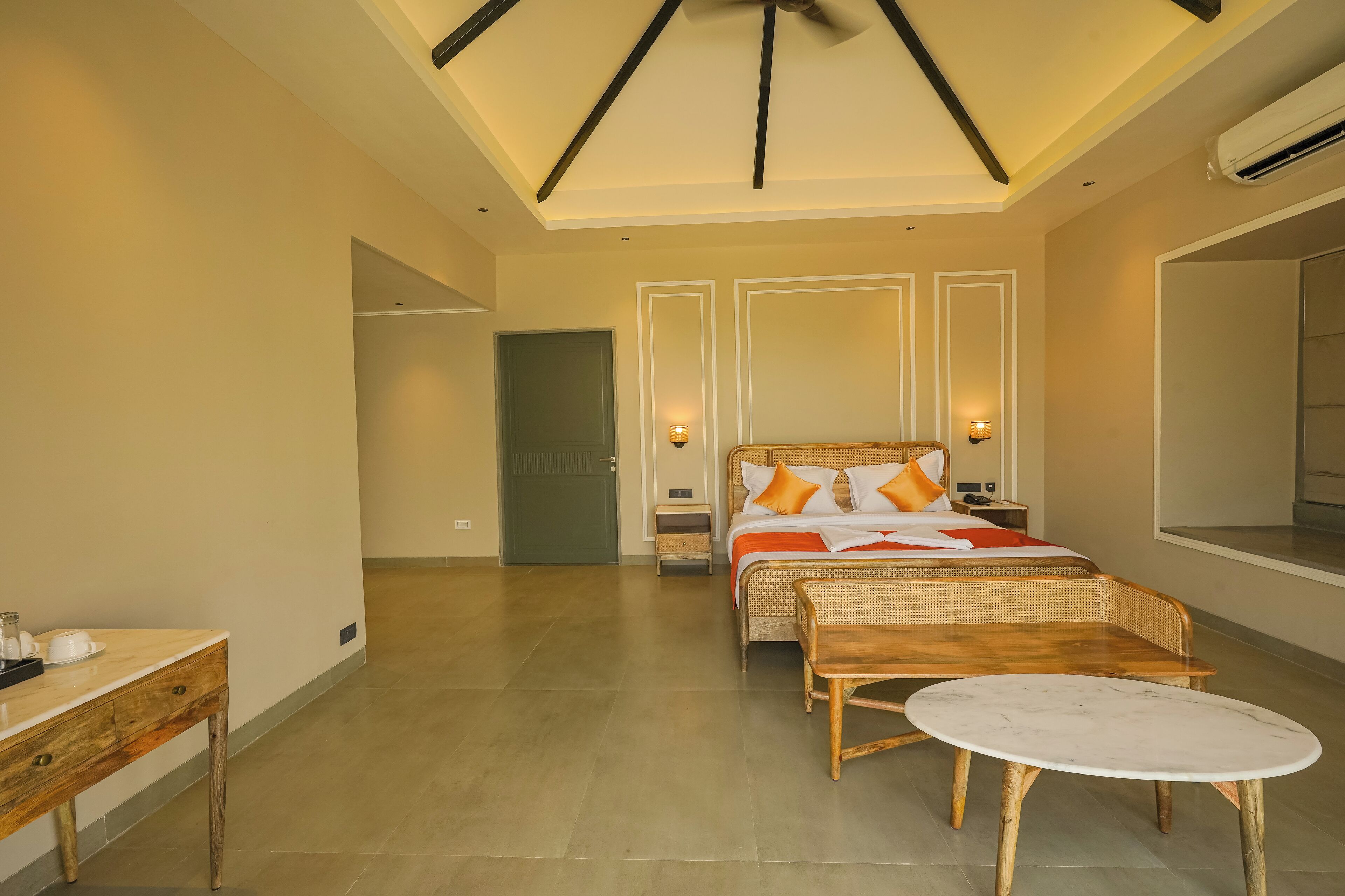 A hotel room with a bed, a small table, a chair, a mirror, and a door.