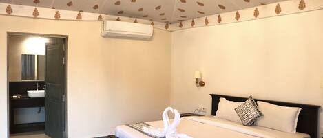 Habitación de hotel con cama, mesita de noche, lámpara de pared y baño con lavamanos y espejo.