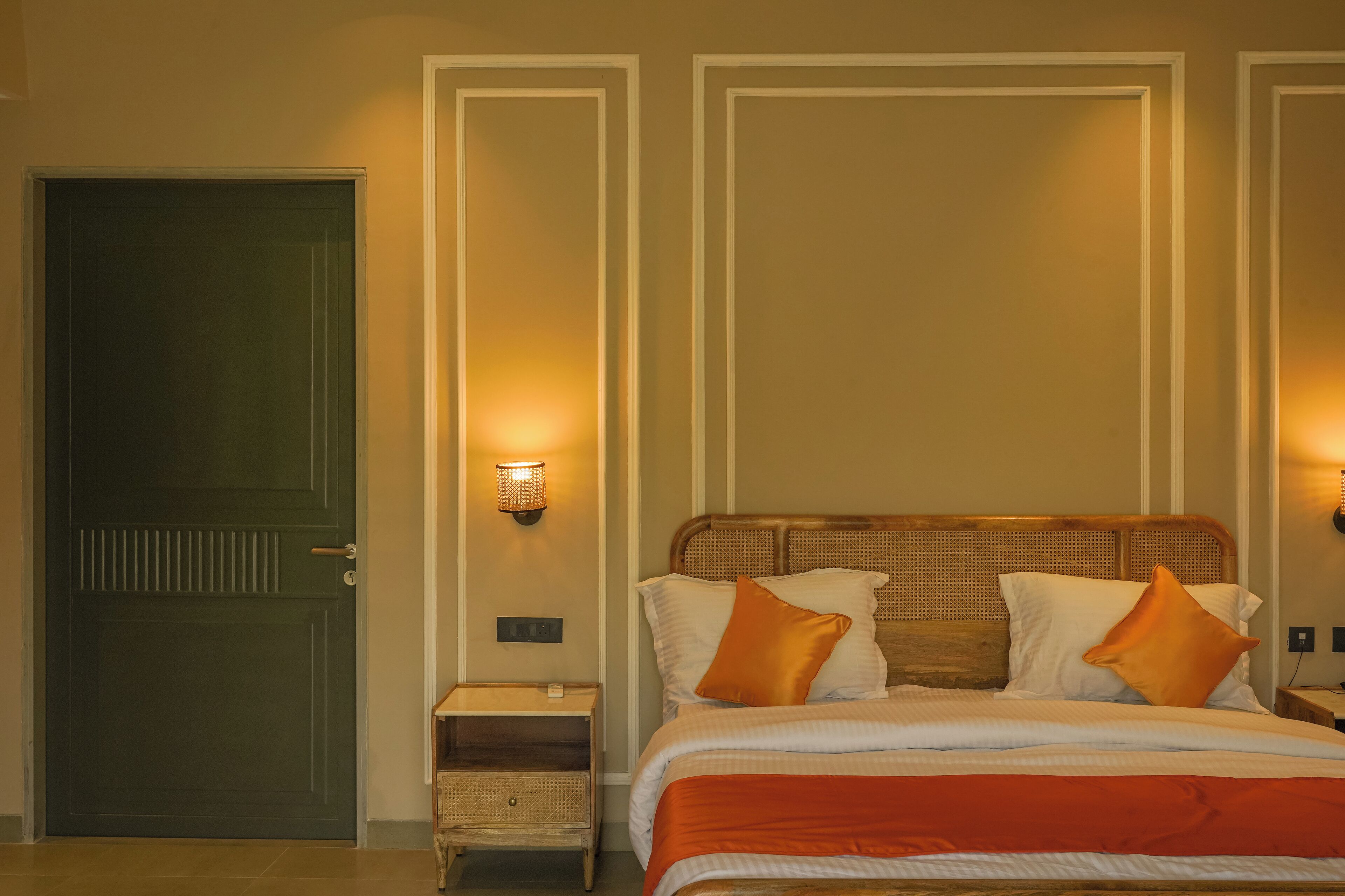 A hotel room with a bed, a nightstand, a wall-mounted lamp, and a door.