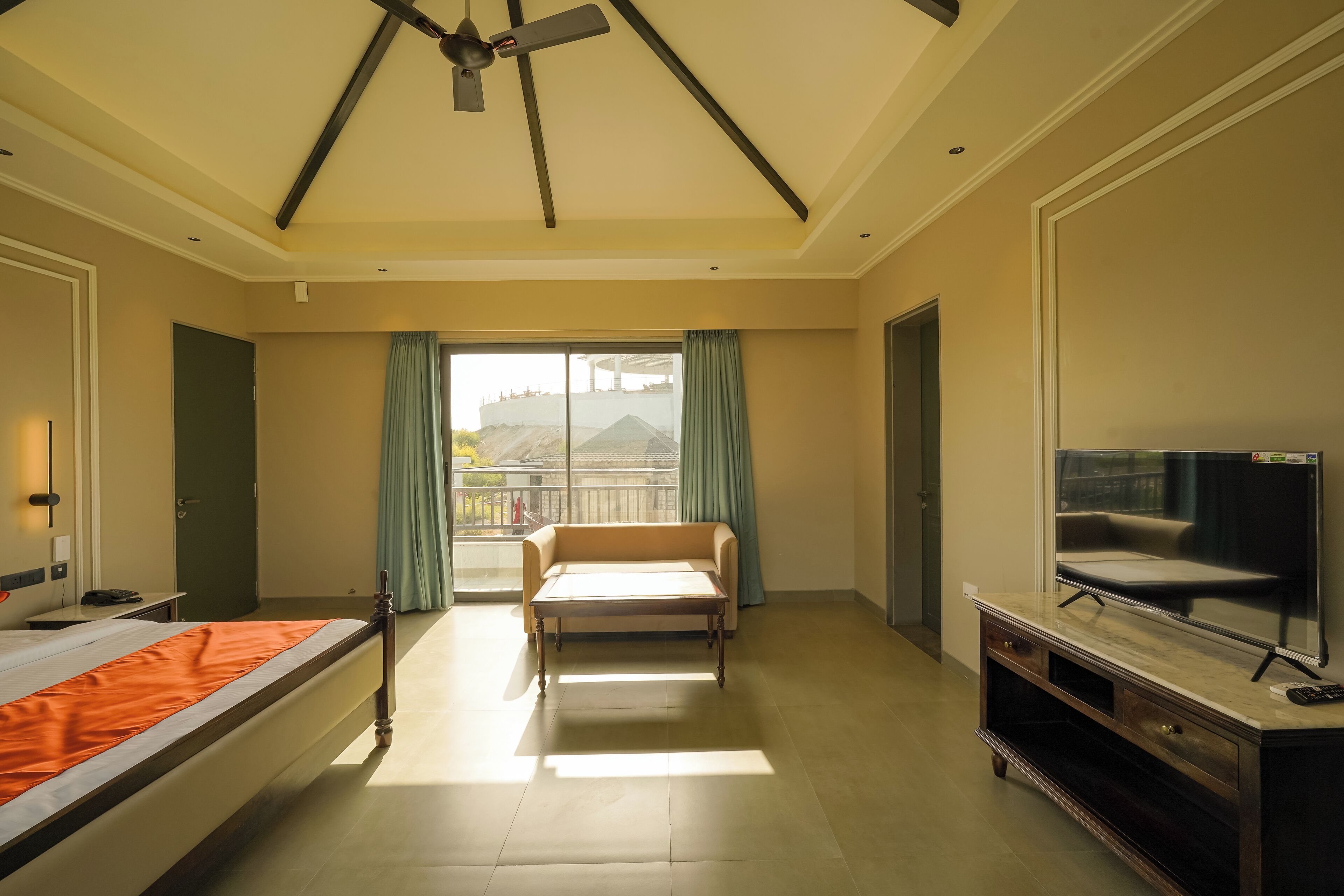 A hotel room with a bed, a sofa, a TV, and a balcony with curtains.