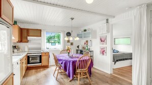 Eine moderne Küche mit Holzausstattung, ein Esstisch mit violetter Tischdecke und ein gemütliches Schlafzimmer mit Bett und Vorhängen.