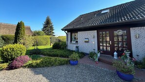 A building with a tiled roof, brick walls, and a well-maintained garden with various plants and a gravel pathway.