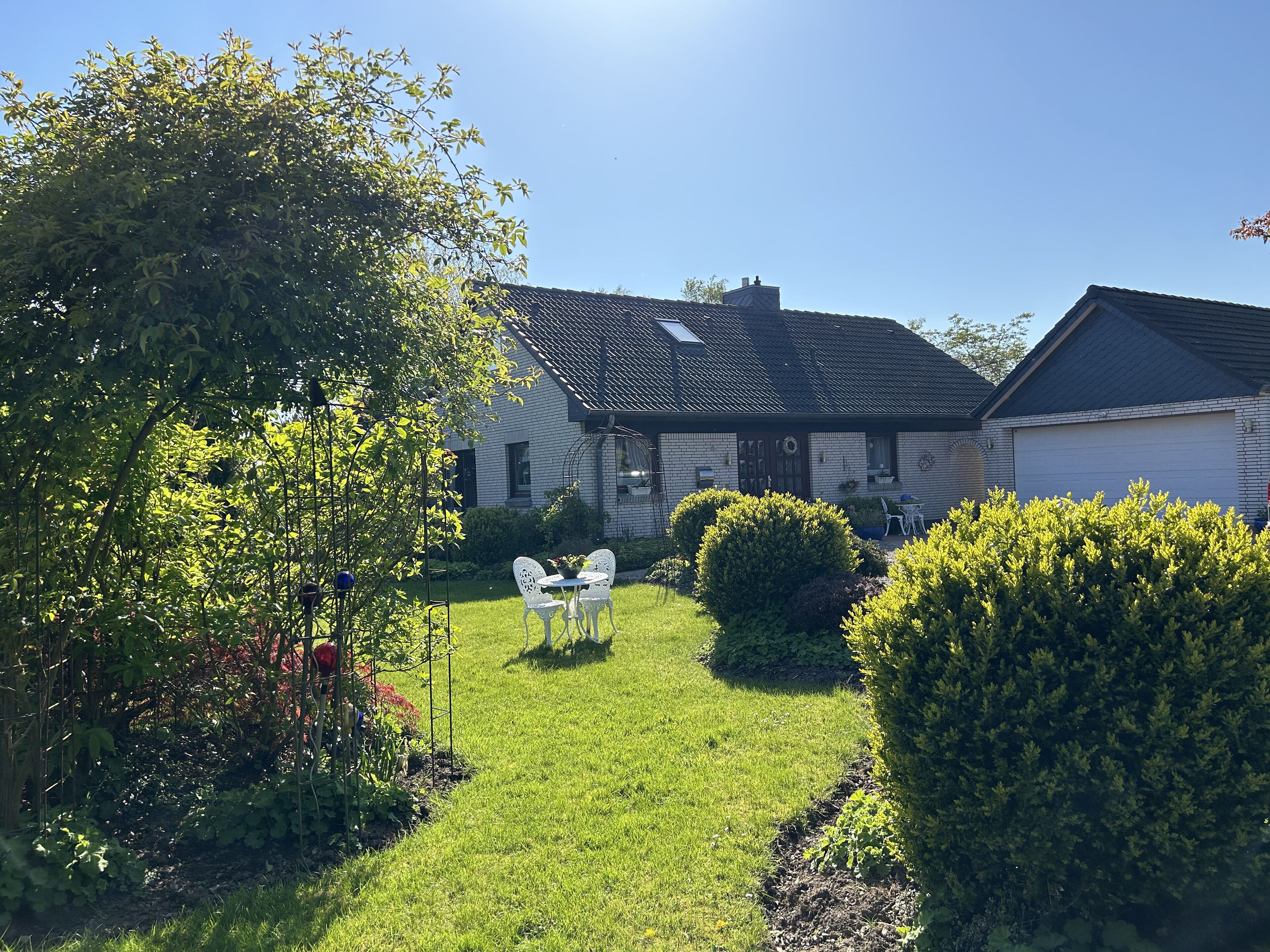 Une maison avec un jardin, une terrasse avec des chaises et un garage.