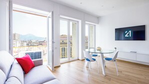 A modern living room with a sofa, a glass table, and chairs, a TV mounted on the wall, and large windows offering a city view. - At Twenty-One: new apartment with exclusive panoramic views! (Napoli)