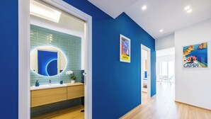 A modern hallway with blue walls, wooden flooring, and a round mirror with a blue accent. - At Twenty-One: new apartment with exclusive panoramic views! (Napoli)