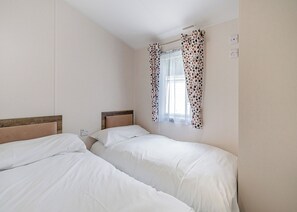 A room with two beds, a window with patterned curtains, and a visible electrical outlet.