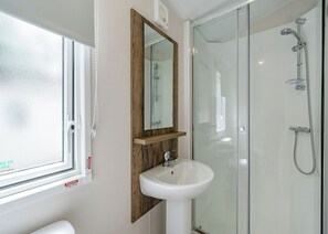 Une salle de bain avec une douche à parois de verre, un lavabo blanc et un miroir encadré en bois.