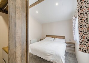 A bedroom with a wooden headboard, a white bedspread, a nightstand, and a radiator. - Caravan with one double and one twin. (Longridge, Ribble Valley)
