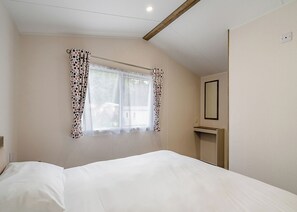 Une chambre avec un lit simple, une fenêtre ornée de rideaux à motifs, une table de chevet et un miroir au mur.