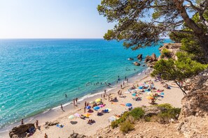 Uma praia com águas turquesa cristalinas, pessoas tomando sol e guarda-sóis.