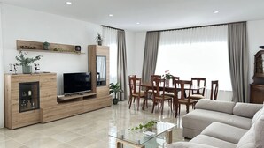Una sala moderna con televisor de pantalla plana, mueble de entretenimiento de madera, mesa de comedor con sillas y un sofá.