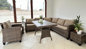 Un área de estar al aire libre amoblada con un sofá de mimbre, una mesa de madera y plantas en macetas.