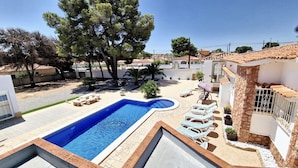 Una piscina con sillas de descanso y un pequeño solárium, rodeada de árboles y un muro de piedra.