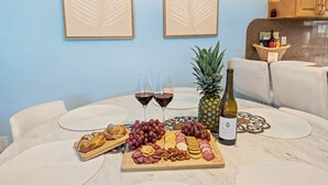 Una mesa de comedor con una tabla de embutidos, dos copas de vino tinto, una botella de vino y una piña.