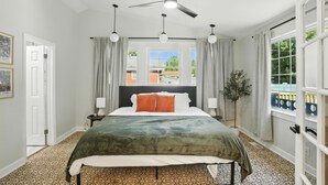 Ein Schlafzimmer mit Bett, Deckenventilator, Fenster, Vorhängen und einer Pflanze.