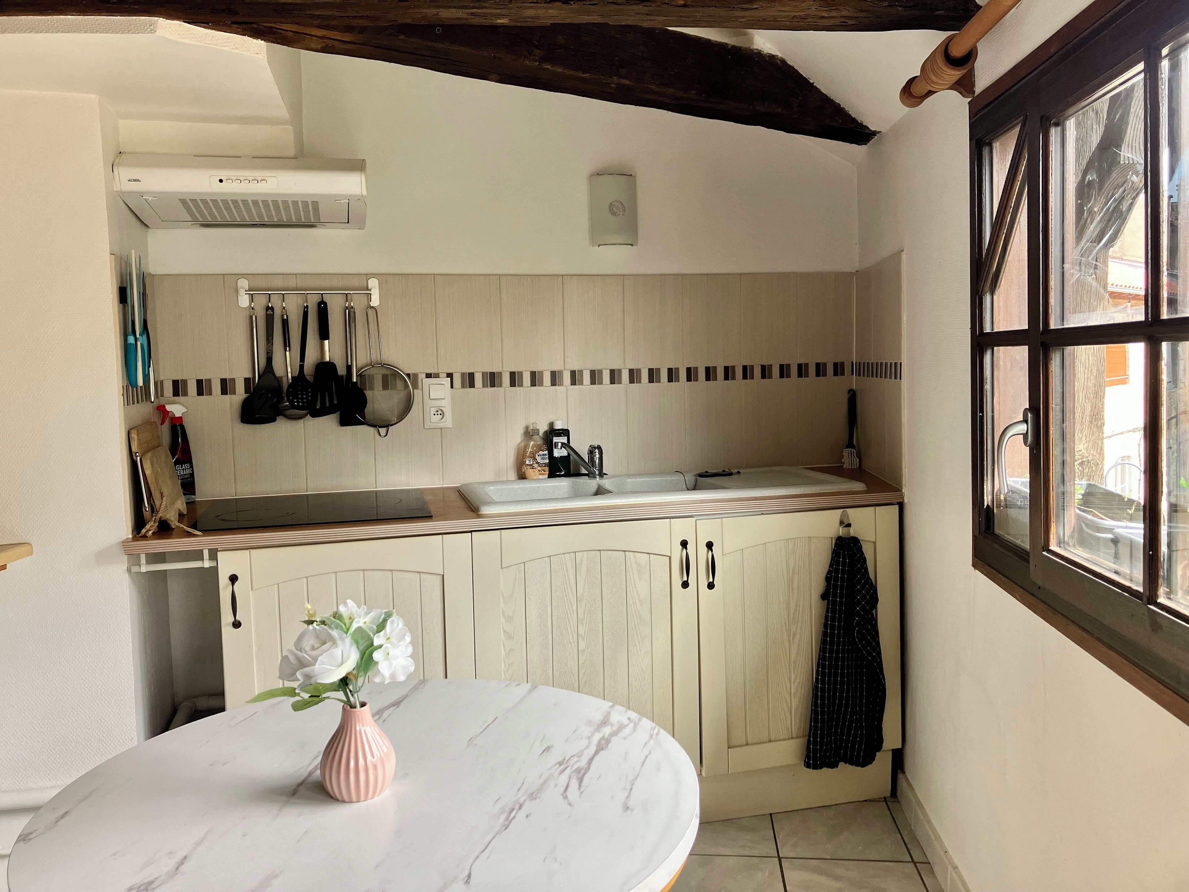 A kitchen with a marble countertop, a sink, hanging utensils, and a window with a view.