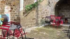A stone courtyard with arches, a table with chairs, and a staircase.