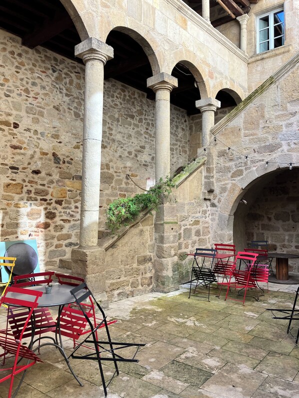 A stone courtyard with arches, a table with chairs, and a staircase.