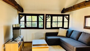 A living room with a sectional sofa, a small white table, a TV on a stand, and a window with multiple panes.