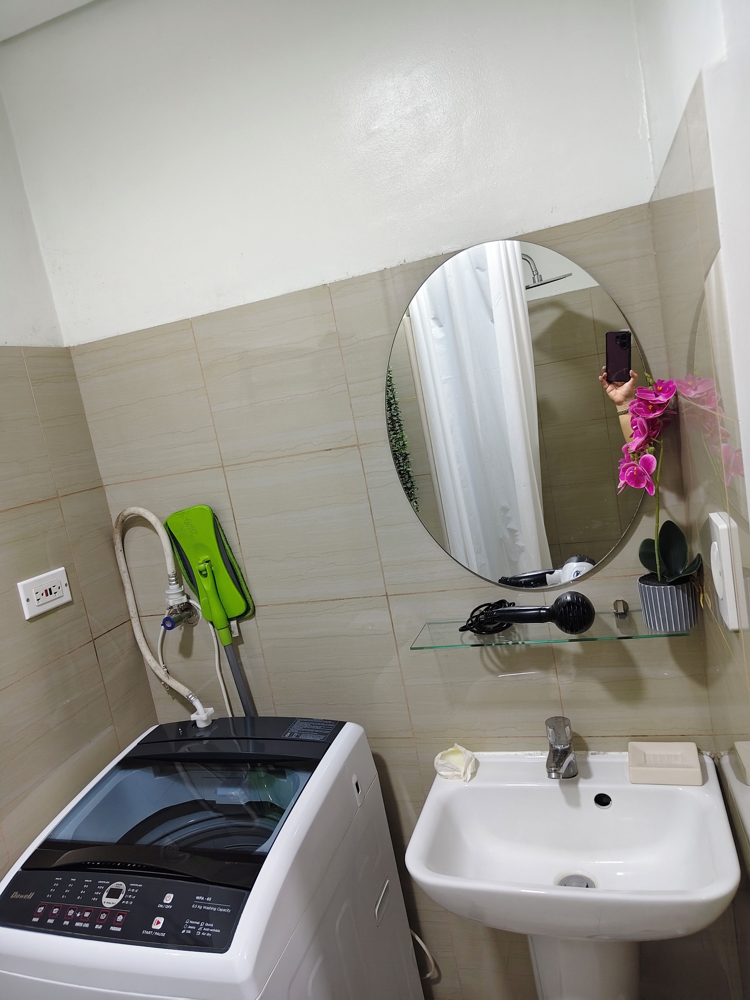Une salle de bain équipée d’un lave-linge, d’un évier, d’un miroir et d’une douche.