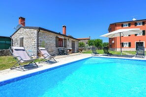 Une piscine avec des chaises longues et un bâtiment en pierre doté d’un toit rouge.