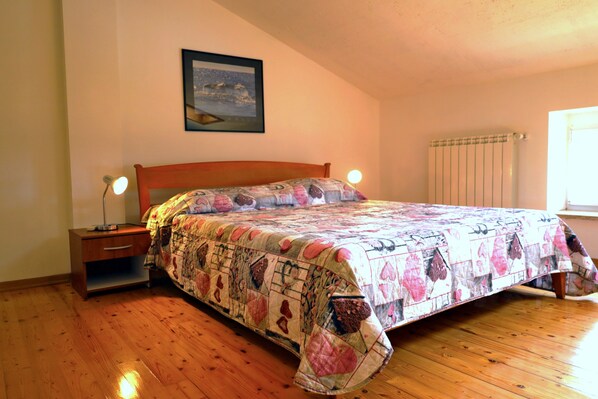 Une chambre avec un lit en bois, une table de chevet, une lampe de chevet, un tableau encadré au mur et une fenêtre avec un radiateur.