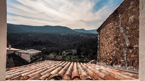 Une vue depuis une terrasse sur le toit, recouverte de tuiles en terre cuite, donnant sur une vallée parsemée de bâtiments et bordée de collines densément boisées.