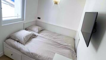 Een slaapkamer met een bed, een bureau, een televisie, een raam en een wandlamp.