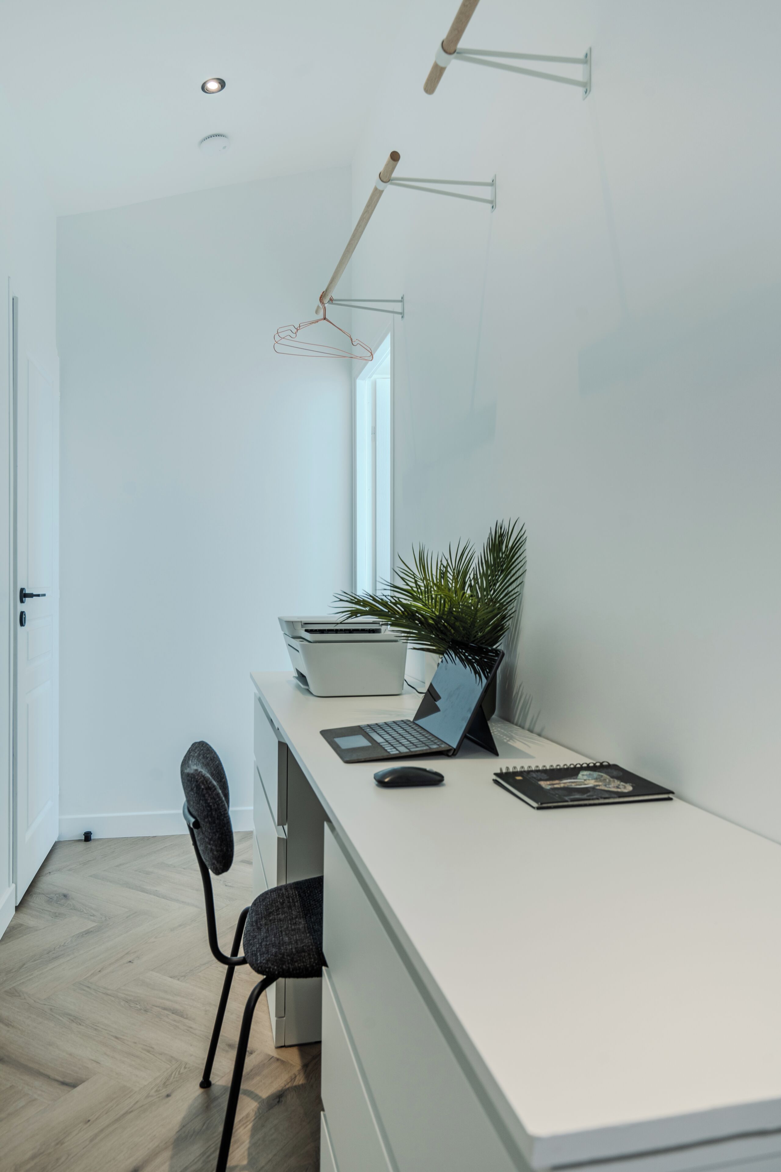 Et moderne kontormiljø med et hvidt skrivebord, en bærbar computer, en plante og en stol.