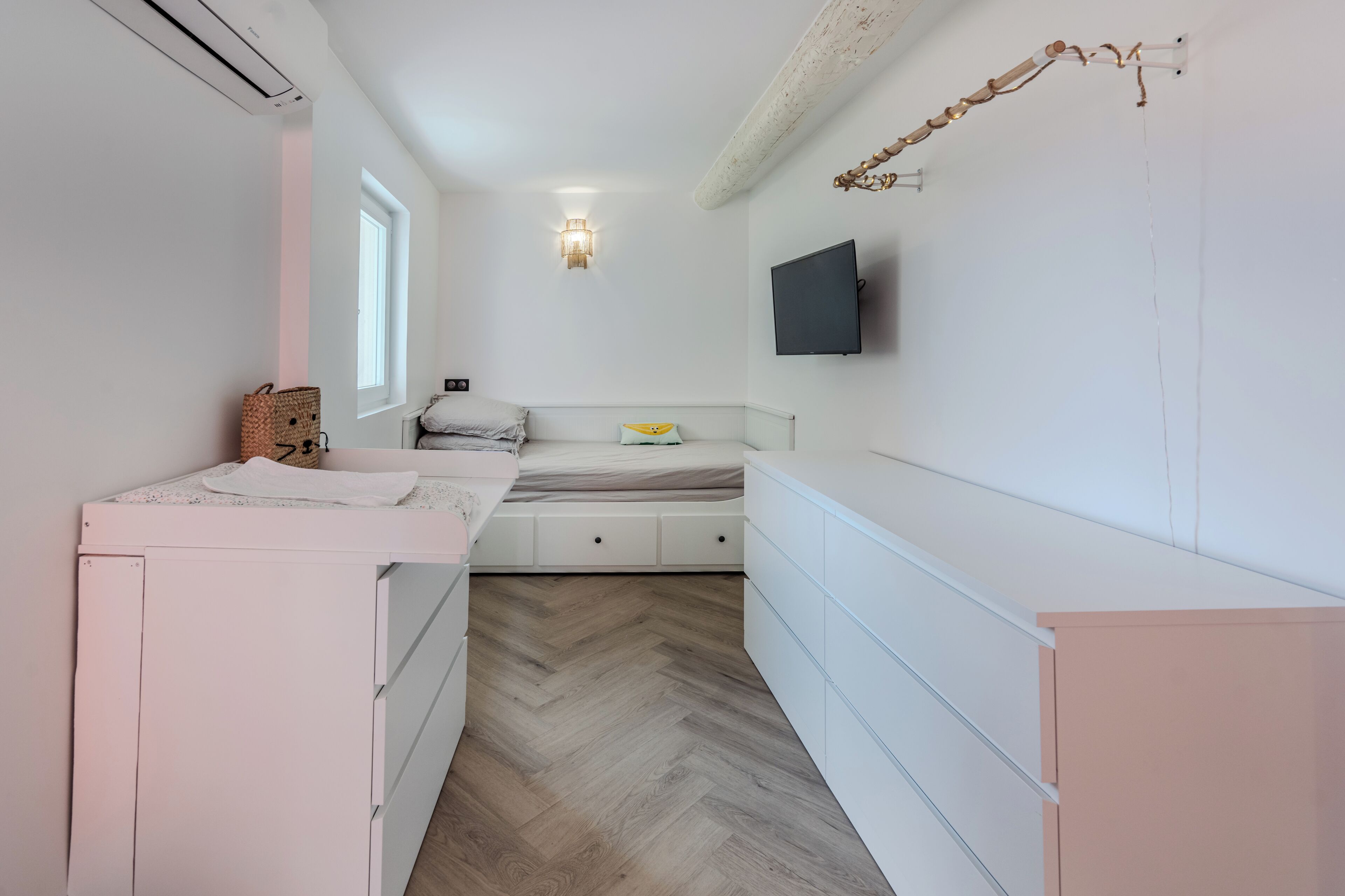 Une chambre à coucher avec un lit, des tables de chevet, un téléviseur fixé au mur et une fenêtre.