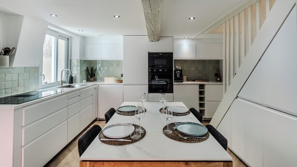 Une cuisine moderne avec des meubles blancs, un îlot central et un coin repas aménagé pour quatre personnes.
