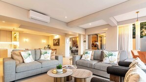 A modern living room with two grey sofas, round coffee tables, and a flat-screen TV.