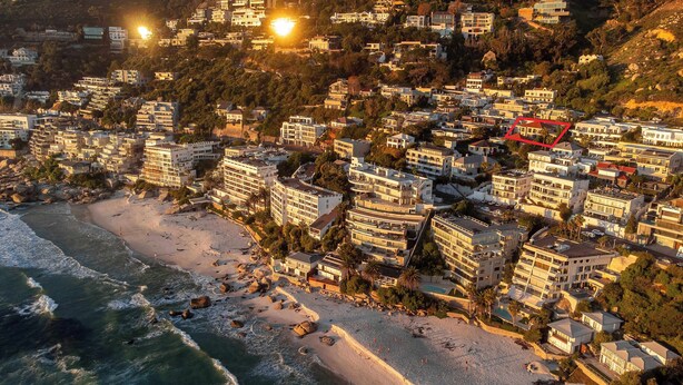 An aerial view of a coastal residential area with beachfront properties, dense housing, and a prominent red outlined area.