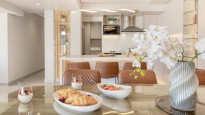 A modern dining area with a glass table, a vase of white orchids, and a bowl of fruit.