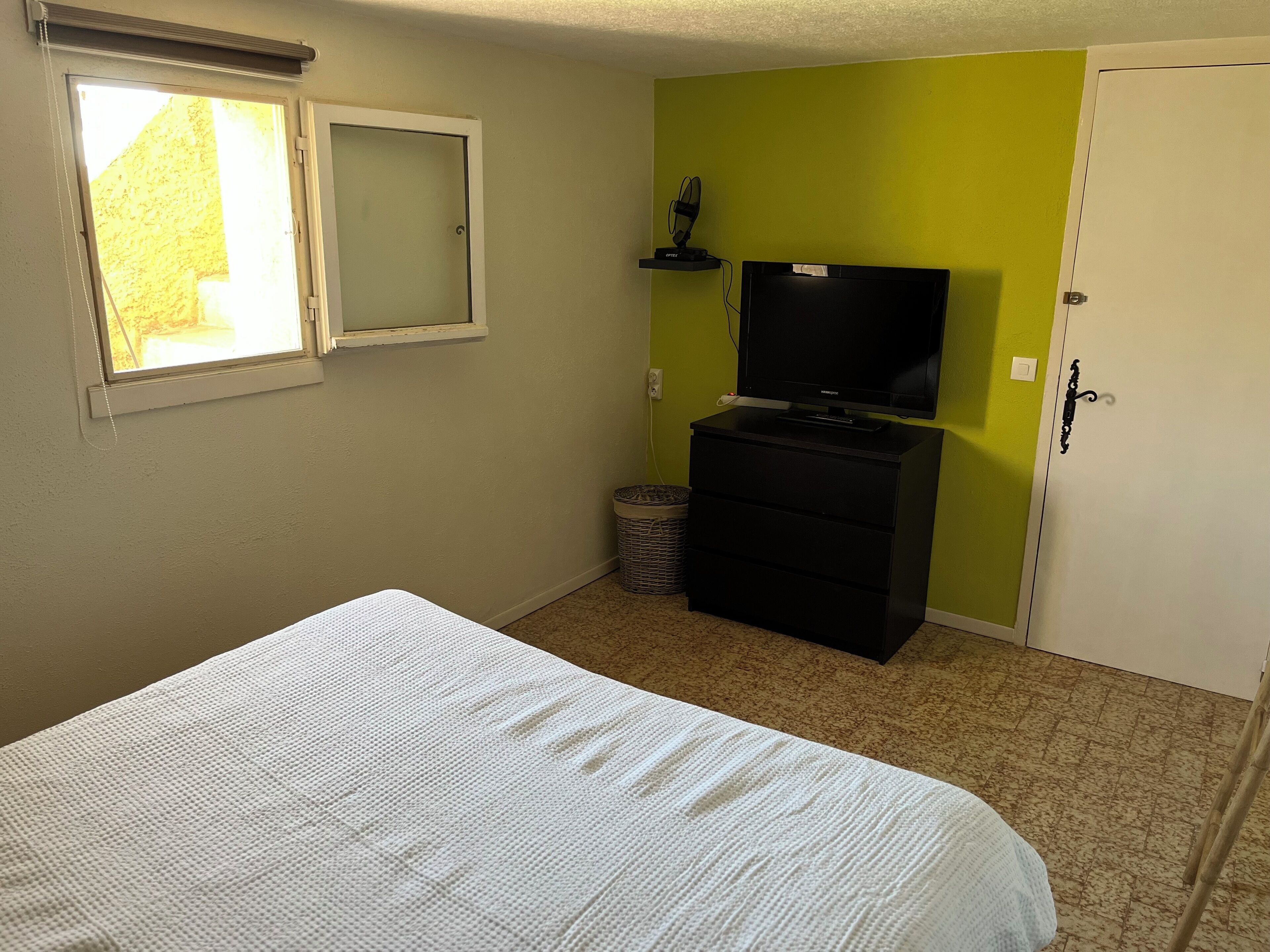 Une chambre à coucher avec un lit, un téléviseur posé sur un meuble, une petite poubelle et une armoire.