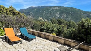 Une terrasse avec deux fauteuils de jardin, une chaise pliante et une table, offrant une vue sur un paysage montagneux.