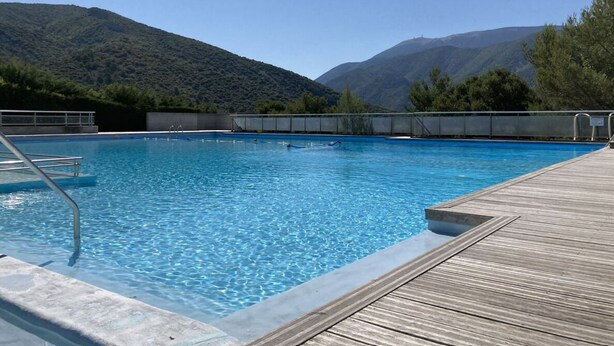Une piscine dotée d’une terrasse en bois, entourée de montagnes.