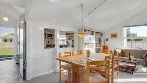Een ruime keuken met witte houten wanden, een eethoek met een houten tafel en stoelen, en een gezellige zithoek met een bank en salontafel.