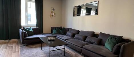 A modern living room with a sectional sofa, a coffee table, and a large mirror on the wall.