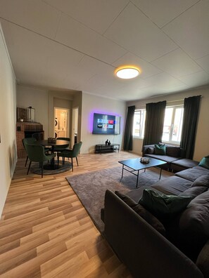Uma sala de estar moderna com televisão de tela plana, uma área de jantar com mesa redonda e cadeiras, um sofá e uma mesa de centro.