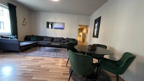 Una sala moderna con un sofá, una mesa de comedor con sillas, un espejo grande y un ventanal con cortinas.