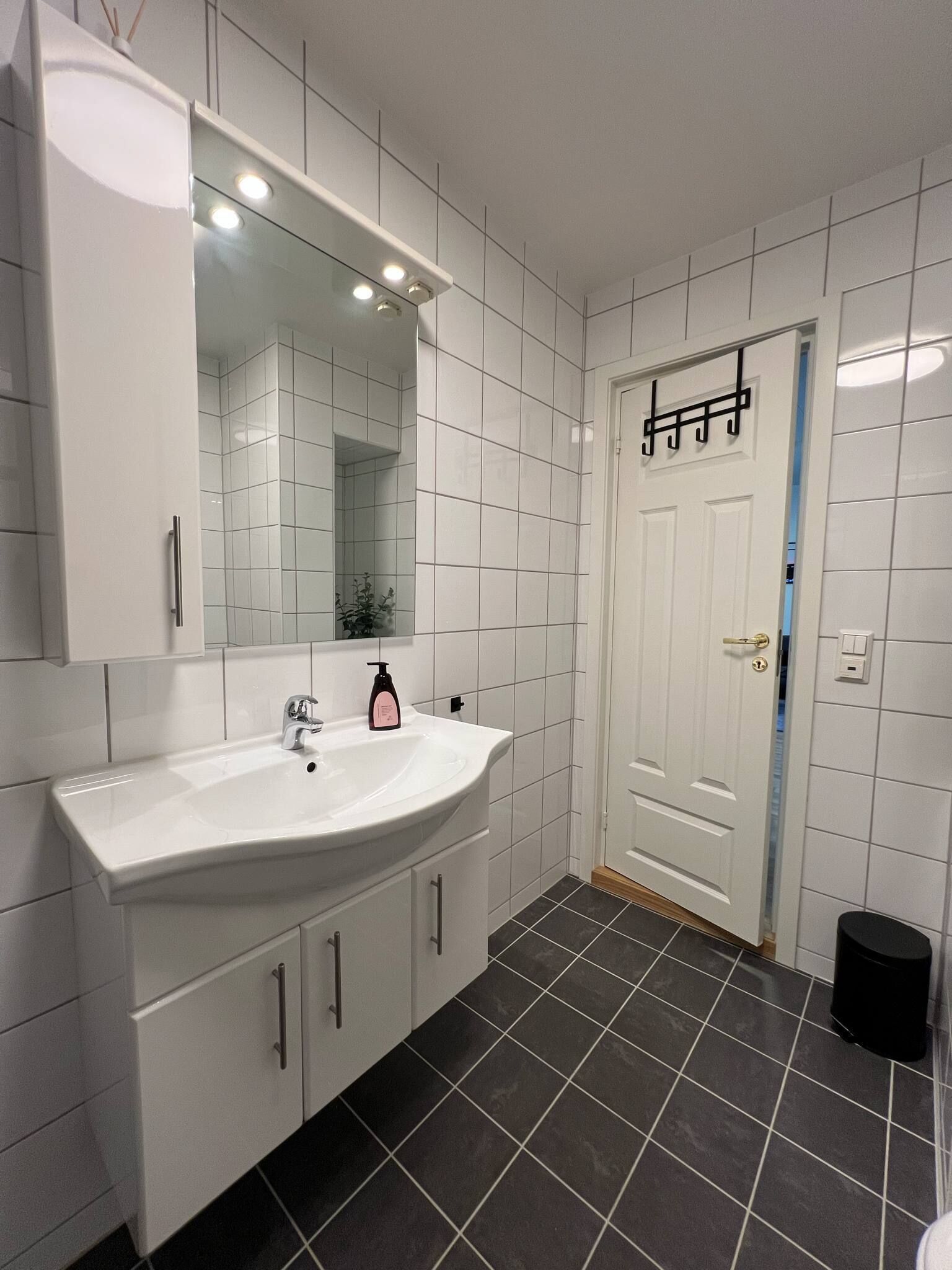 Un baño con azulejos blancos, un lavamanos blanco y un espejo encima.