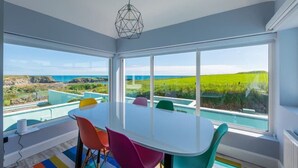 A modern dining room with a large table and colorful chairs, large windows with a view of a pool and landscape. - The Granary Loft at Annestown House (Annestown)