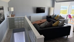 A modern living room with a black sofa, a coffee table, and a TV mounted on the wall. - The Granary Loft at Annestown House (Annestown)