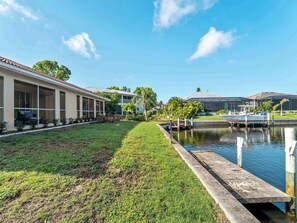 A waterfront property with a grassy lawn, a dock, and a building with large windows. - Punta Gorda Isles Villa On The Waterfront (Punta Gorda)