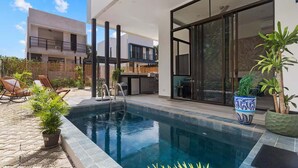 A modern outdoor pool area with a clear blue pool, lounge chairs, and potted plants.