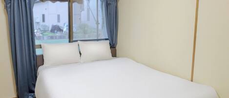 Una habitación de hotel con una cama grande, suelo de madera, unidad de aire acondicionado y ventana con cortinas.